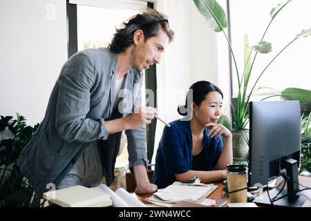 Male architect discussing with female colleague using computer at home office Stock Photo