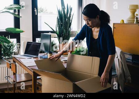 Mature female architect opening cardboard box at home office Stock Photo