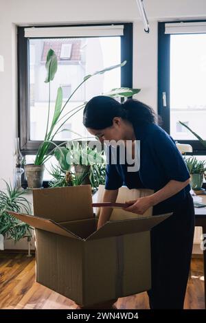Mature female architect with plank and cardboard box at home office Stock Photo