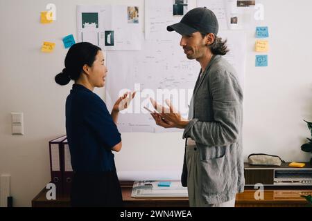Multiracial architect colleagues discussing in front of blueprint on wall at home office Stock Photo