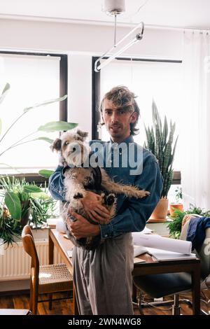 Portrait of male architect carrying dog standing at home office Stock Photo