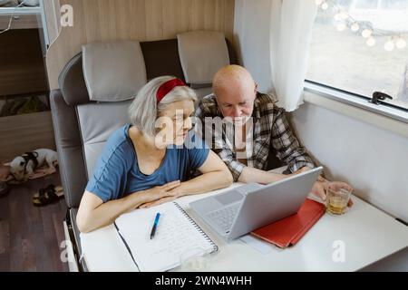 Curious senior couple sitting with laptop at table in camper van Stock Photo