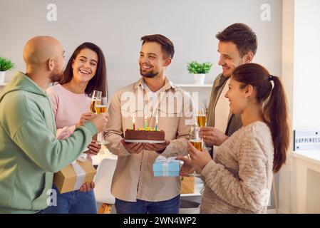 Happy Young Man Celebrates Birthday Surrounded By Friends With Cake And Gifts Stock Photo