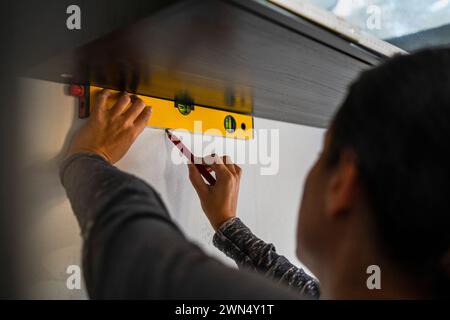 Female carpenter using bubble level and marking on wall with pencil Stock Photo