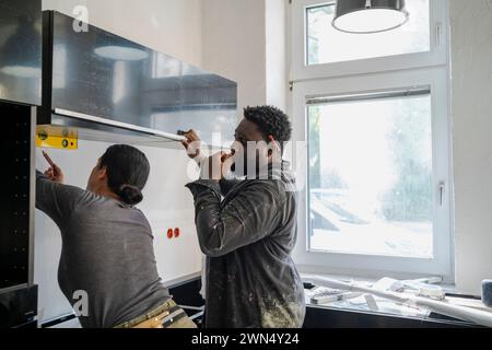 Diverse male and female carpenters working together in kitchen at apartment Stock Photo