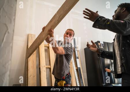 Multiracial male carpenters carrying plank while working in apartment Stock Photo