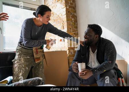 Multiracial male and female carpenters talking during coffee break in apartment Stock Photo