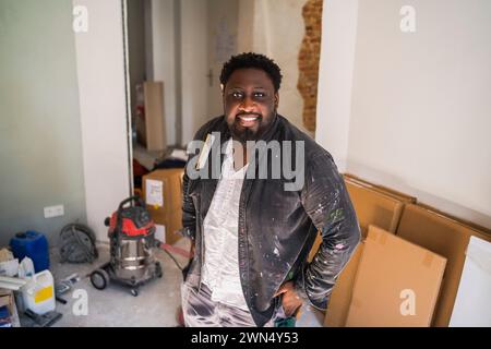 Portrait of smiling male carpenter standing with hand in pocket at apartment Stock Photo