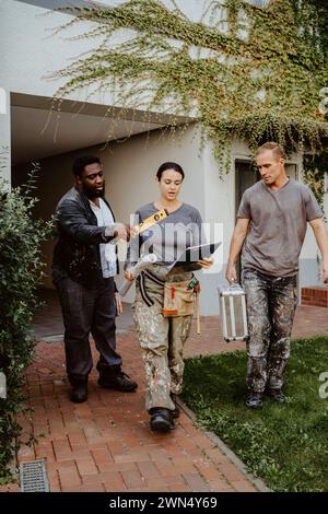 Female construction manager discussing with workers while walking outside house Stock Photo