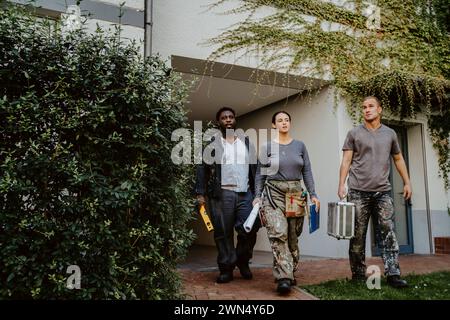Confident female construction manager walking with workers outside house Stock Photo