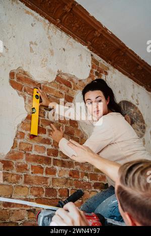 Man assisting woman in measuring brick wall while renovating home Stock Photo
