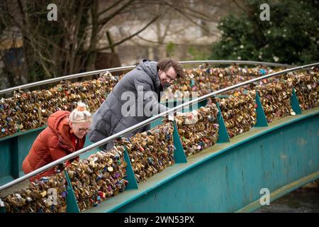 24/03/21   Mollie Edge and Jake Mycock search for and read inscriptions on the padlocks.  The Ôlove lockÕ Weir Bridge over the river Wye in Bakewell. Stock Photo