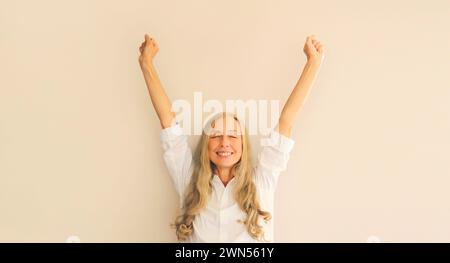 Happy lucky woman employee manager in office shirt having fun or feels victory raising her hands up at work Stock Photo