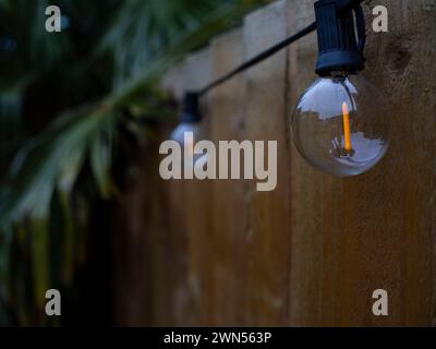 A vintage bulb string lights hanging in a backyard, close to night time. street lamp in the night. Light bulbs decoration with selective focus - bokeh Stock Photo