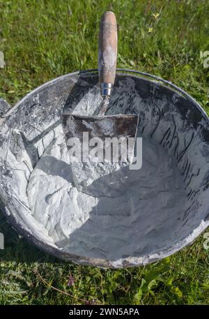 Bucket full white adhesive mortar ready for applicate. Green grass as background Stock Photo