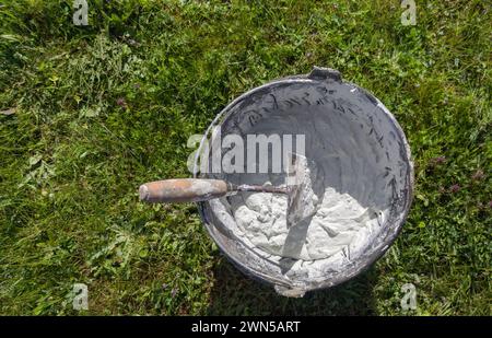 Bucket full white adhesive mortar ready for applicate. Green grass as background Stock Photo