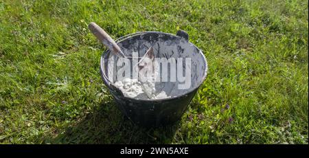 Bucket full white adhesive mortar ready for applicate. Green grass as background Stock Photo