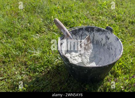 Bucket full white adhesive mortar ready for applicate. Green grass as background Stock Photo