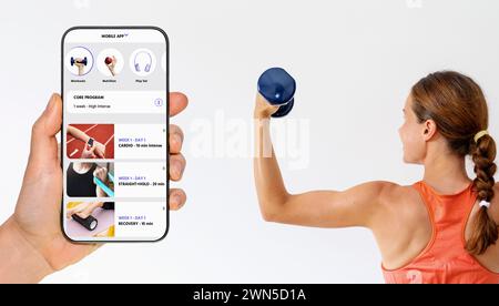 Personal digital fitness coach mobile app interface on screen of smartphone next to sporty woman holding dumbbell. Stock Photo