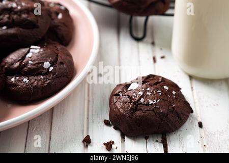 Delicious snack of homemade brownie cookies with cracked top and sprinkled salt flakes on the table and a little bottle of milk. Close up Stock Photo