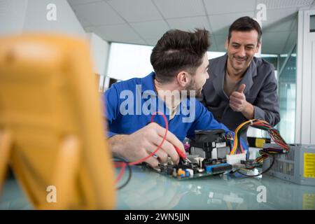 boss giving thumbs up to apprentice technician using multimeter Stock Photo