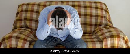 Image of a man sitting on a sofa while covering his ears and not wanting to hear anyone. Anxiety and depression problems. Stock Photo