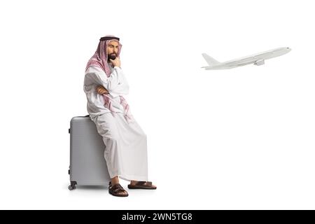 Saudi arab man sitting on a suitcase and waiting for a flight isolated on white background Stock Photo