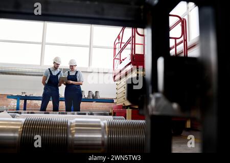 Long shot of male and female technicians working in modern factory using digital tablet and discussing plan, copy space Stock Photo
