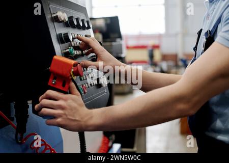 Unrecognizable young male specialist working in factory operating CNC machine Stock Photo