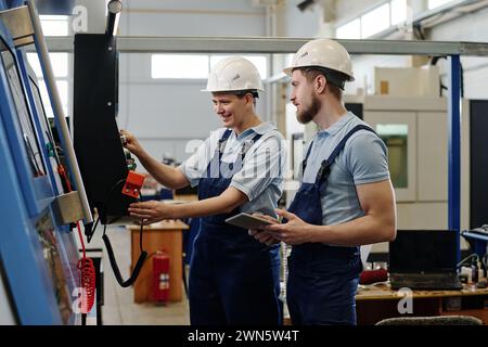 Medium shot of two young male and female factory workers wearing uniform troubleshooting CNC machine Stock Photo