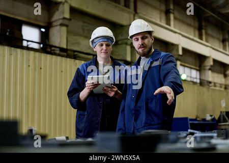 Medium shot of male and female colleagues working in plant warehouse discussing problems Stock Photo