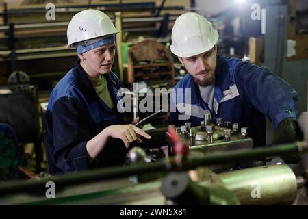 Medium shot of man and woman using old-fashioned industrial equipment in workshop Stock Photo