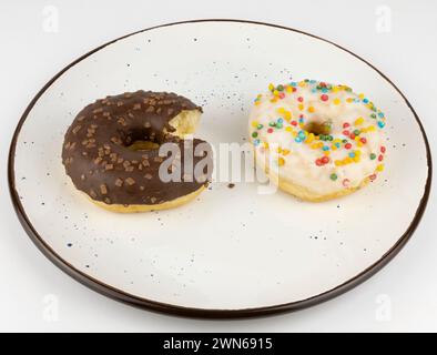 Donuts on a plate. Two chocolate donuts made of white and milk chocolate on a white plate. The concept of being overweight. A chocolate donut with a Stock Photo