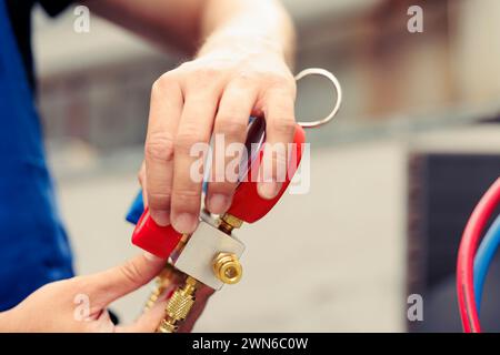 Competent mechanic doing annual condenser maintenance, assembling manifold meters before starting work. Skilled engineer reading pressure of liquids and gases in air conditioning system, close up Stock Photo