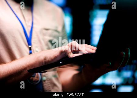 Meticulous technician doing checkup, inputing data on tablet of needed fixes in server hub housing advanced data storage infrastructure supporting critical IT workloads, close up Stock Photo