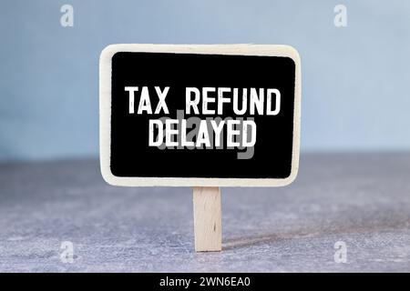 Sticky note with the text Tax Refund Delayed on Income Tax form background with calculator. Stock Photo