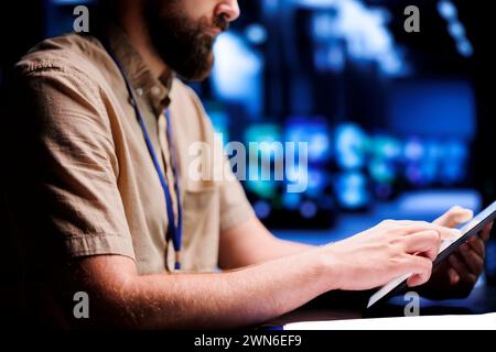 Certified electrician using tablet to examine blade servers for power fluctuations. Licensed professional monitoring data center devices, identifying potential vulnerabilities, close up Stock Photo