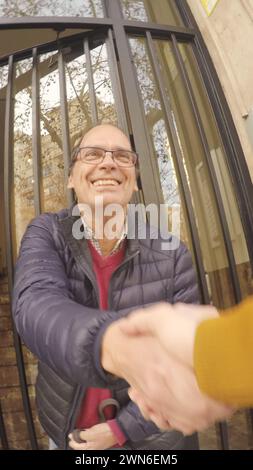 pov happy and very smiling shaking hands with older friend in glasses saying goodbye after walking the dog in a doorway in broad daylight Stock Photo