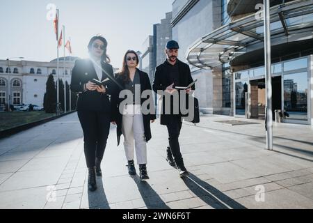 Three young business people confidently walk in the city while engaging in a collaborative work discussion. Stock Photo