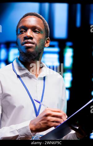 African american professional running server hub diagnostic tests to find and fix data center equipments problems. Engineer looking over maintenance checklist, monitoring critical systems Stock Photo
