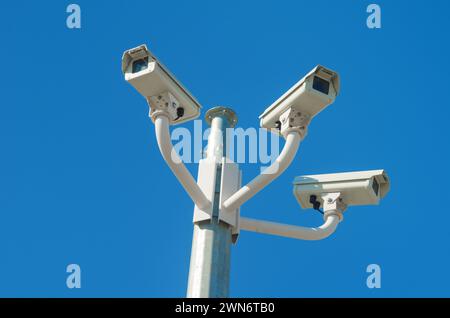 Three security CCTV cameras mounted on a pole against blue sky Stock Photo