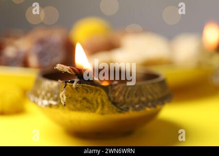 Happy Diwali. Diya lamp on yellow table against blurred lights, closeup Stock Photo