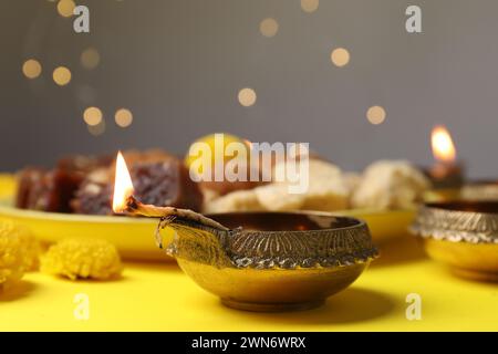 Happy Diwali. Diya lamp on yellow table against blurred lights, closeup Stock Photo