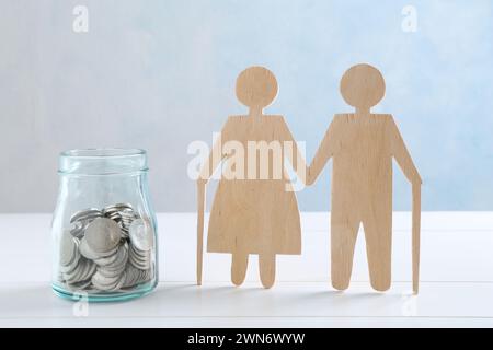 Pension savings. Figure of senior couple and jar of coins on white wooden table Stock Photo