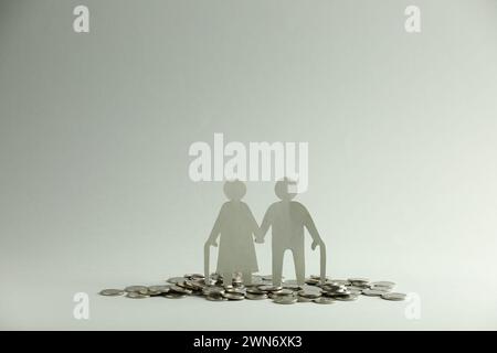 Pension savings. Figure of senior couple and coins on grey background Stock Photo