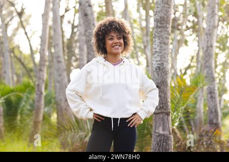 Young biracial woman stands confidently outdoors on a hike, hands on hips Stock Photo