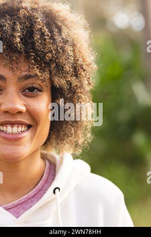 Young biracial woman smiles warmly on a hike, her curly hair framing her face Stock Photo