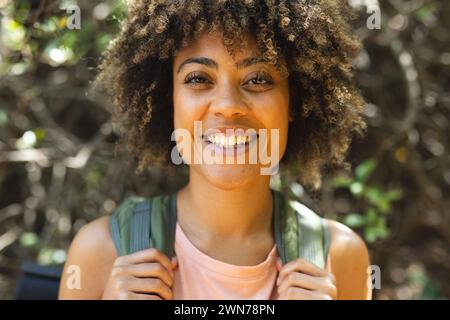 Young biracial woman smiles brightly, standing outdoors with greenery in the background on a hike Stock Photo