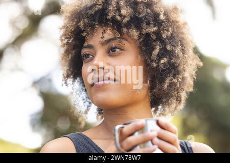 A young biracial woman with curly hair holds a cup outdoors Stock Photo