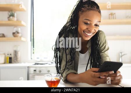 A young African American woman smiles while using her smartphone Stock Photo